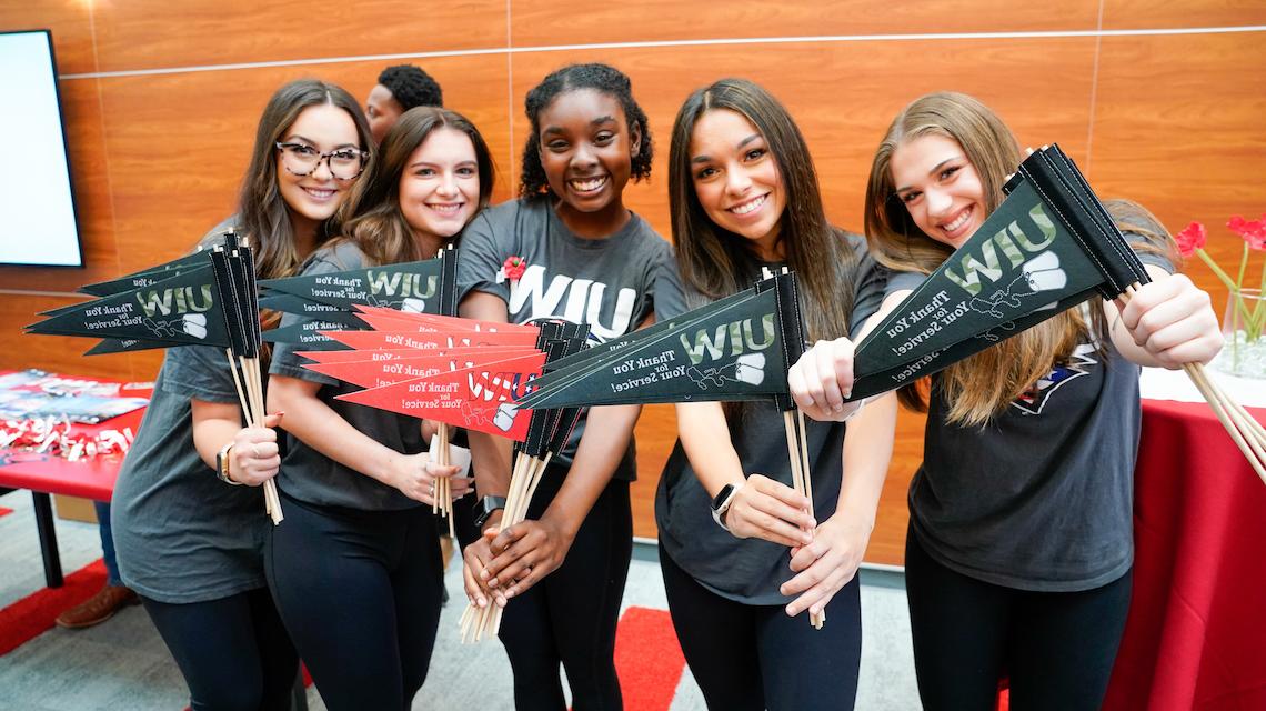 Group of five UIW students holding Thank you for your service pennants 
